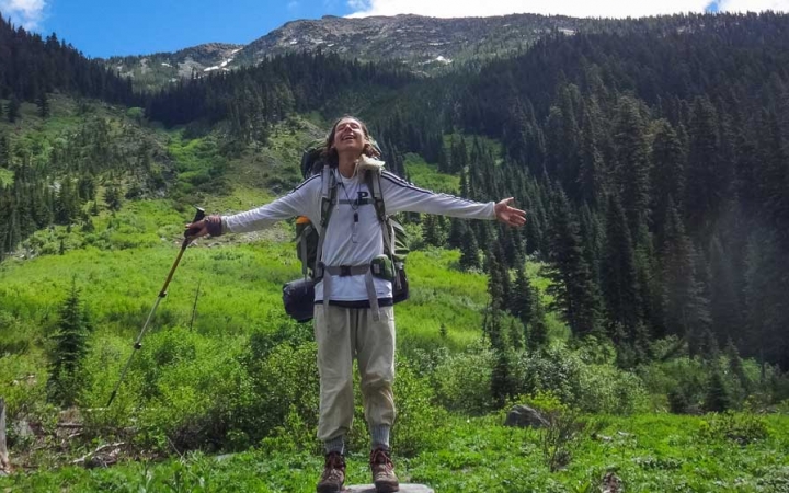 a backpacker spreads their arms out wide with a green mountain landscape in the background